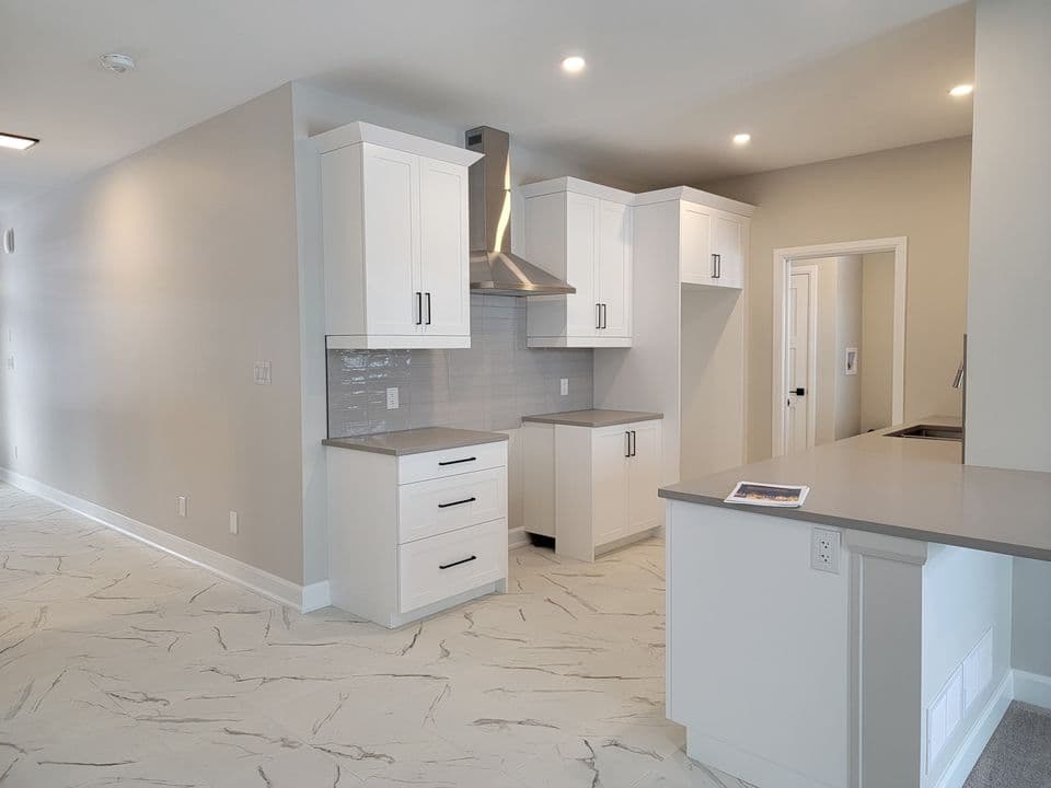 Kitchen with white soft-close cabinetry, stainless hood fan and quartz counters